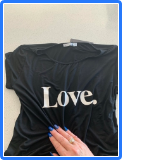 Black tshirt with LOVE in big white letters and a female hand with blue nails touching it 