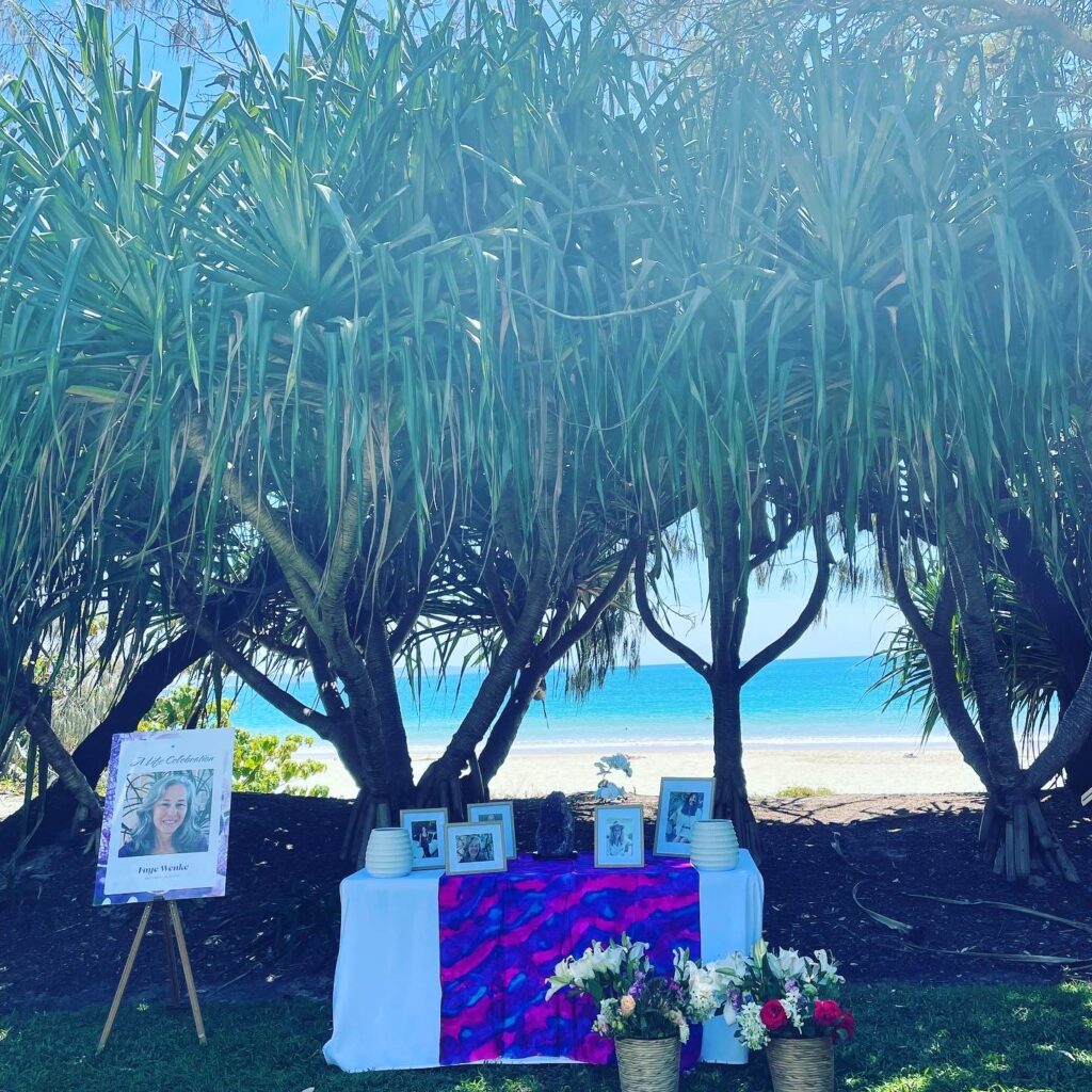 Celebration of life ceremony on the beach with pandanus treees, complete with large photo on an easel, photo display and flowers 