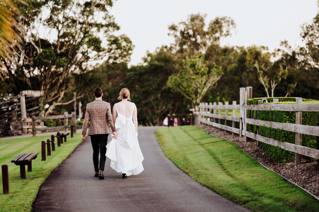 Bride and groom holding hands and walking down a pathway away from the camera