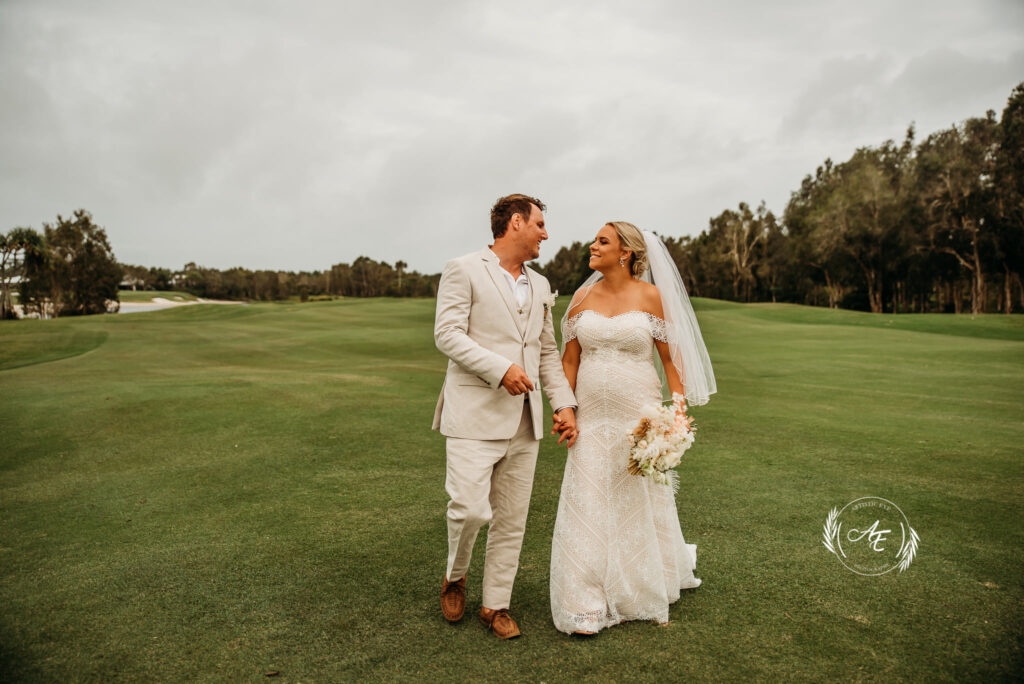 Bride and groom walking on golf course holding hands and smiling at each other