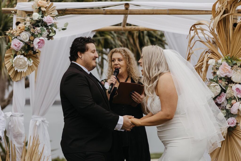 Bride laughing aloud while holding groom's hands with Lynette Maguire marriage celebrant