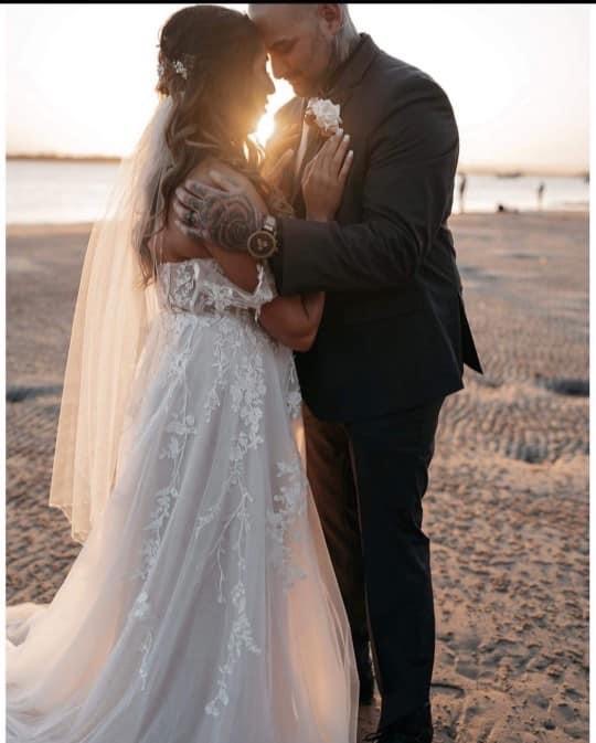 Bride and groom embrace on a beach as the sun sets