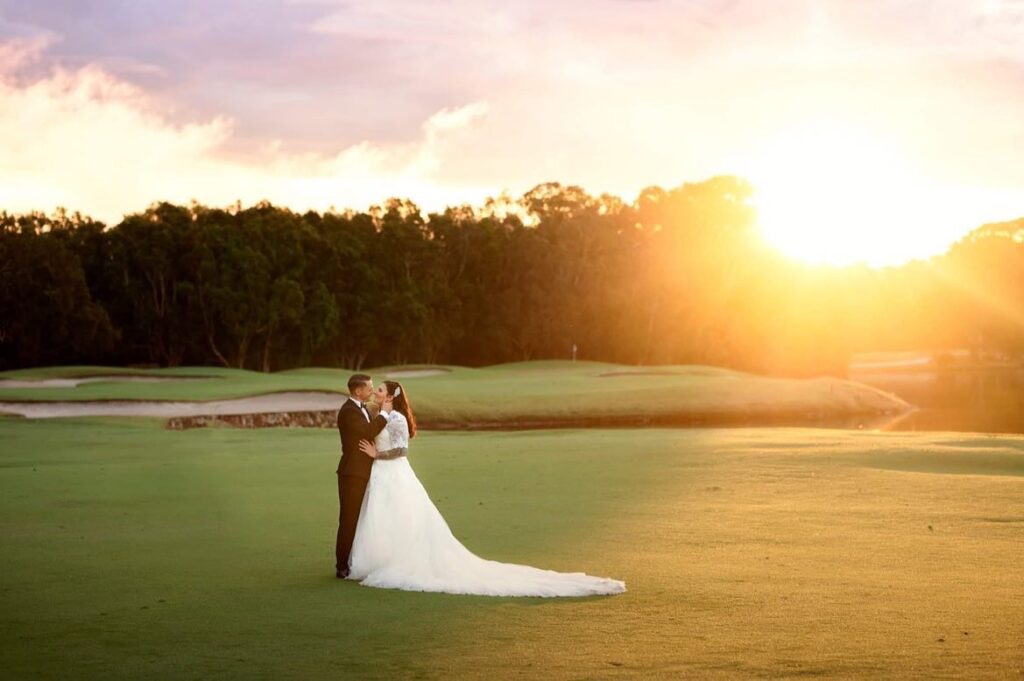 Bride and groom kissing on a golf course as the sun sets