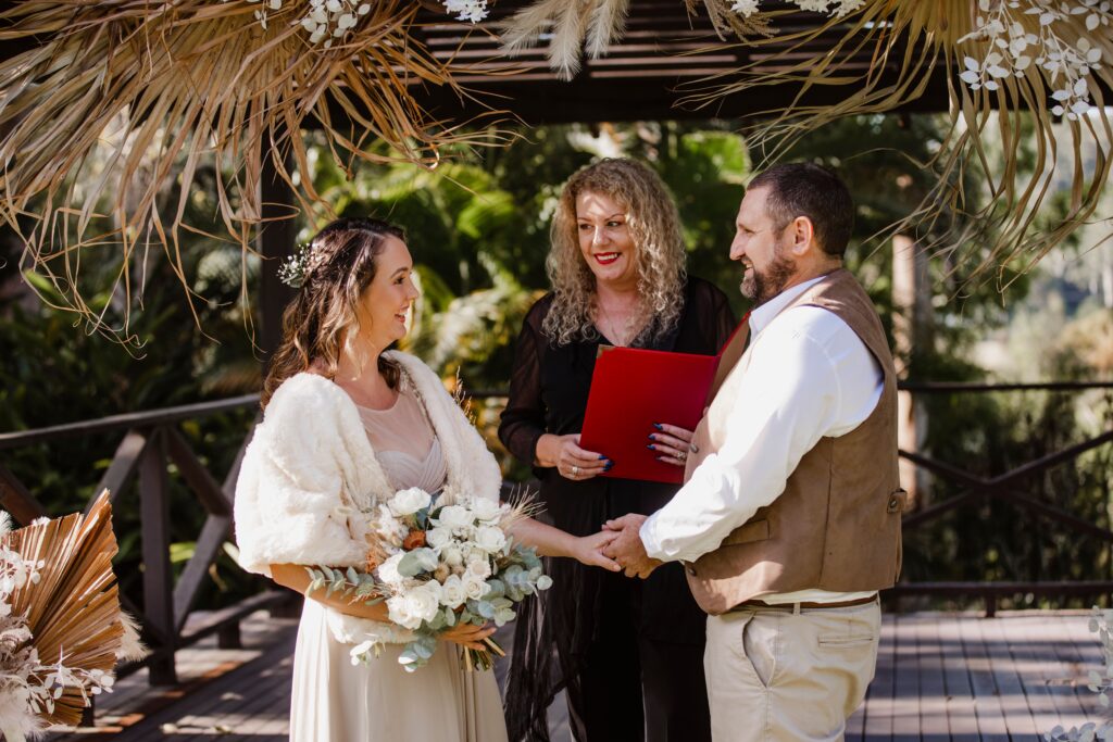 Bride and groom holding hands and facing each other and Lynette maguire marriage celebrant officiating