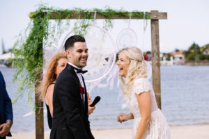 Bride and groom laughing aloud on white beach with still water Kawana Island with Lynette Maguire marriage celebrant