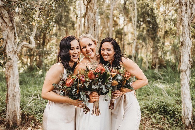 A smiling bride and her to smiling bridemaids each holding Australian native bouquets 