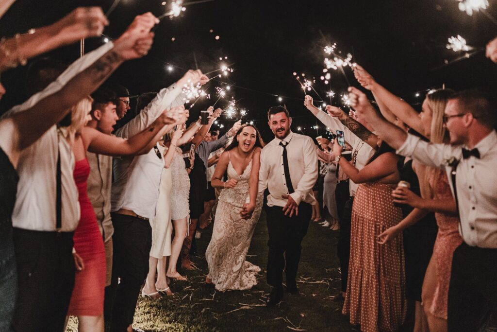 Bride and groom laugh as they run through a tunnel of sparklers held by their guests