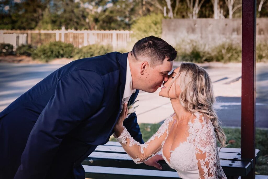 Groom leaning down to kiss his bride who is sitting 