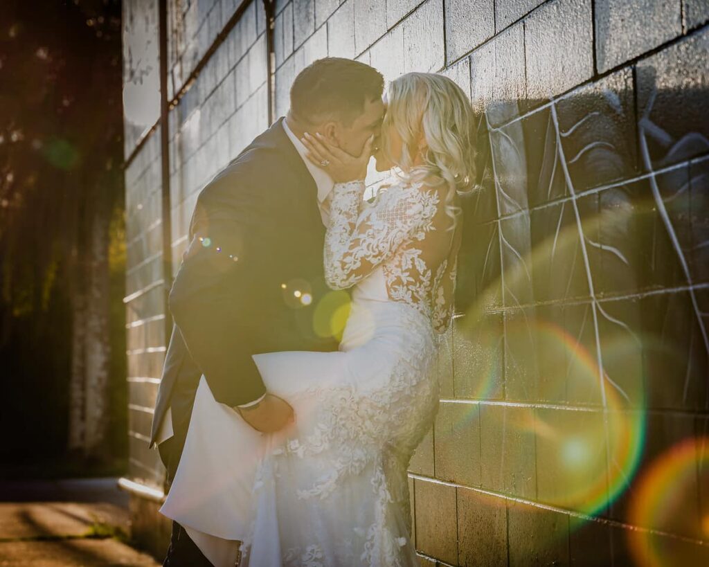 Getting steamy - Groom kissing bride against a brick wall in the afternoon sunlight