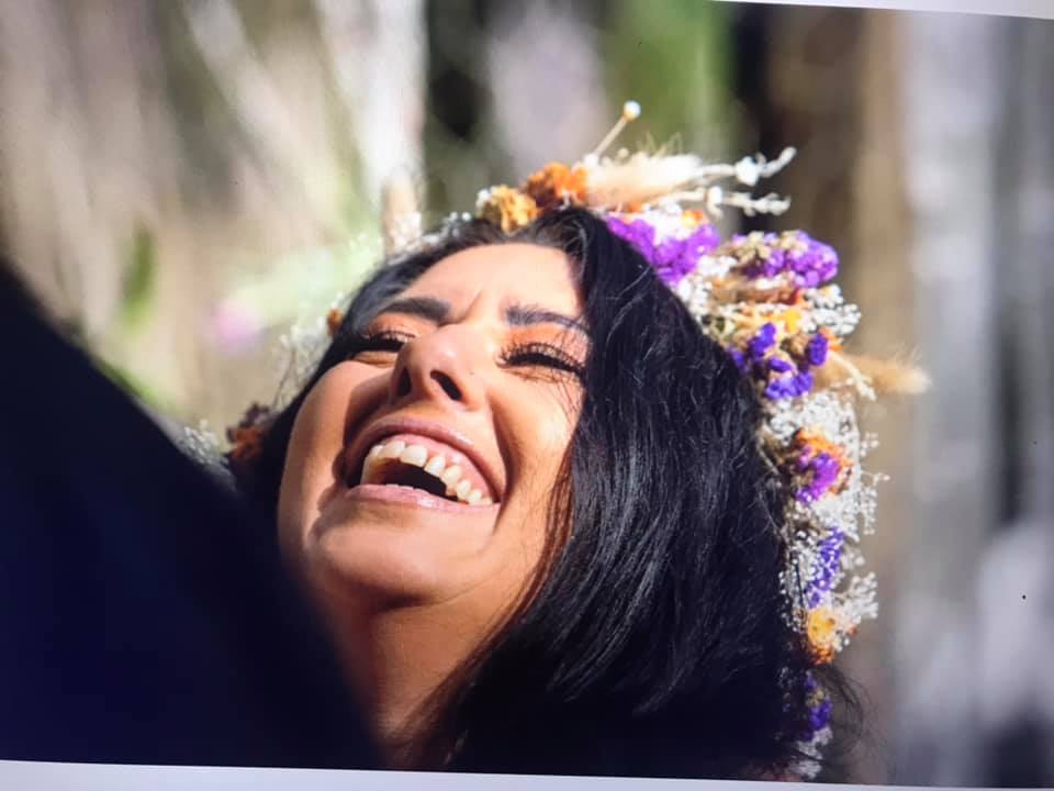 Closeup of bride with floral crown laughing out loud, head back eyes closed