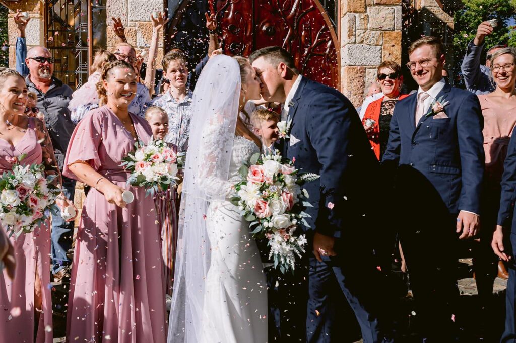 Bride and groom kissing in front of The Chapel, Montville with guests