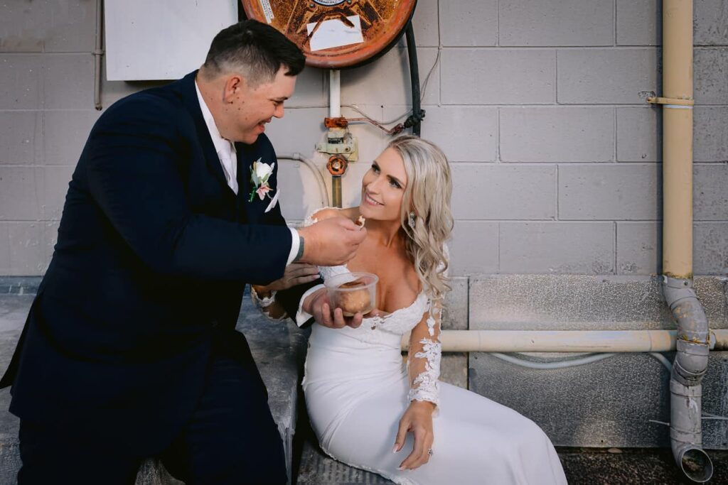 Bride and groom sitting at their old hang out place complete with old fire hose and rusty pipes 