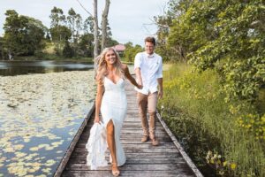 Smiling bride and groom walking along a wooden path with water on the left and bushland on the right 