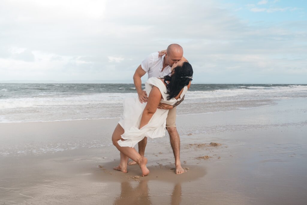 Groom kisses his bride with a dip on a beach with rolling waves