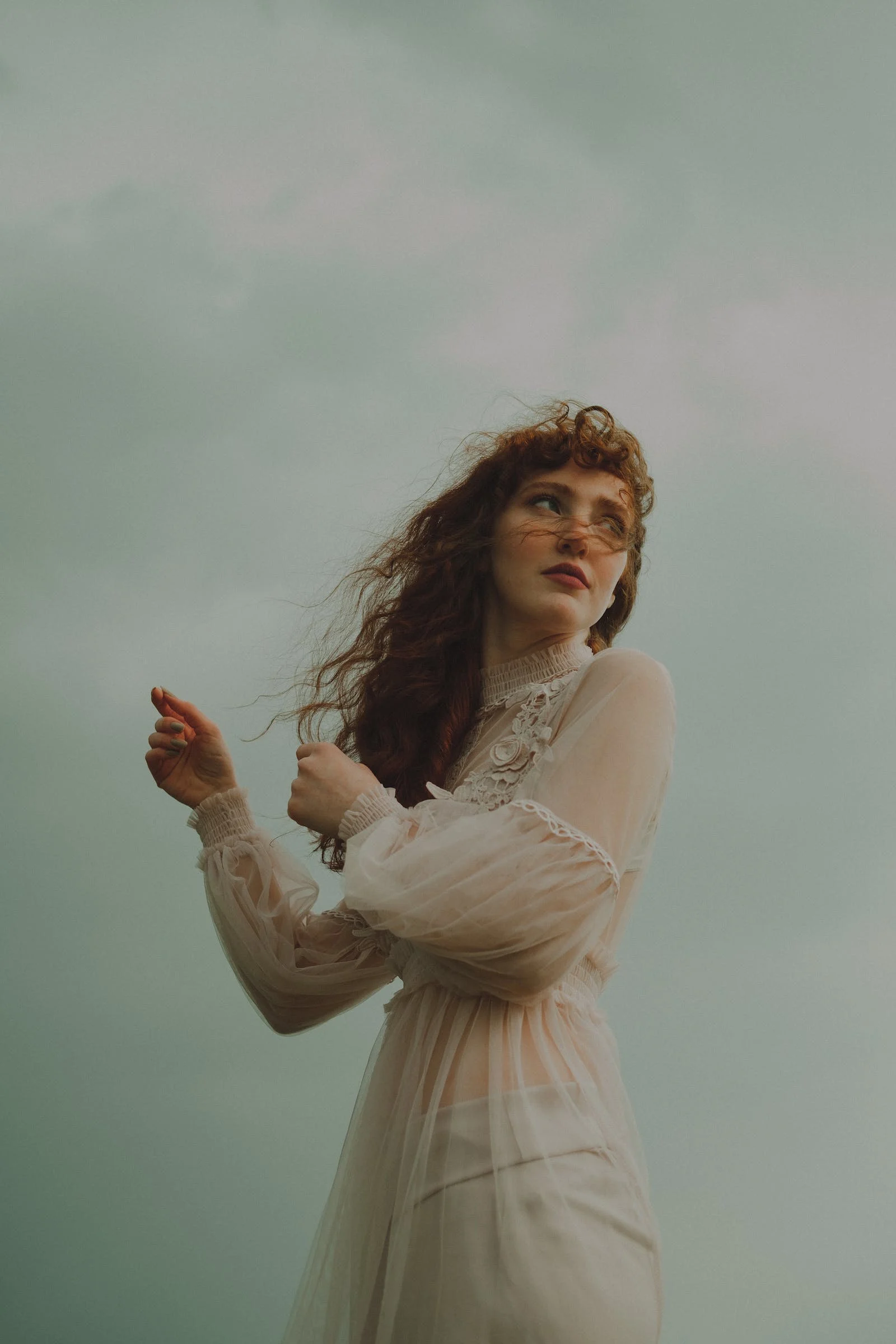 redhaired woman in flowing gown hair blowing in the wind, she looks away from the camera 