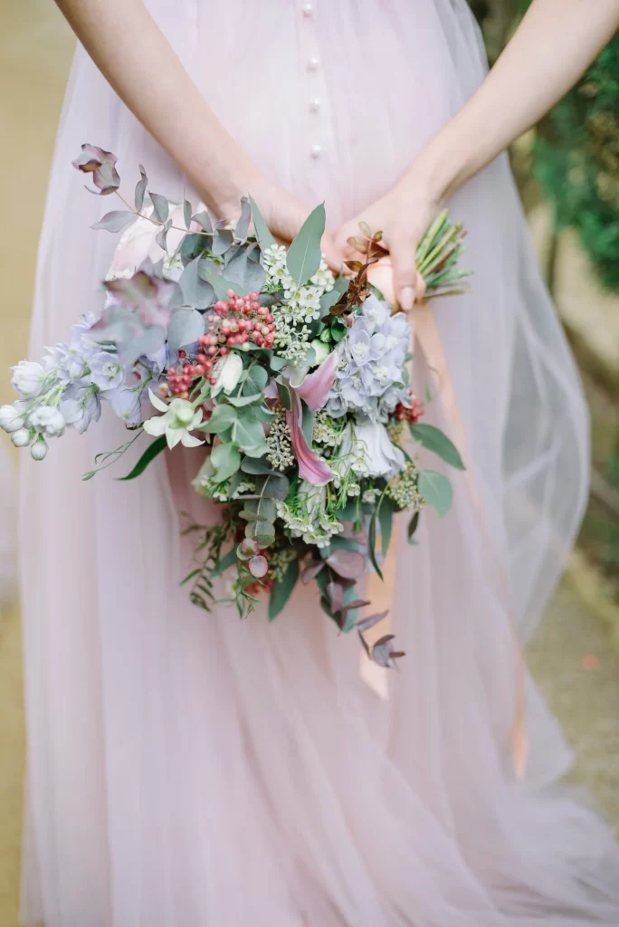 Bridesmaid's torso from the back, flowing violet gown holding bouquet of colourful flowers