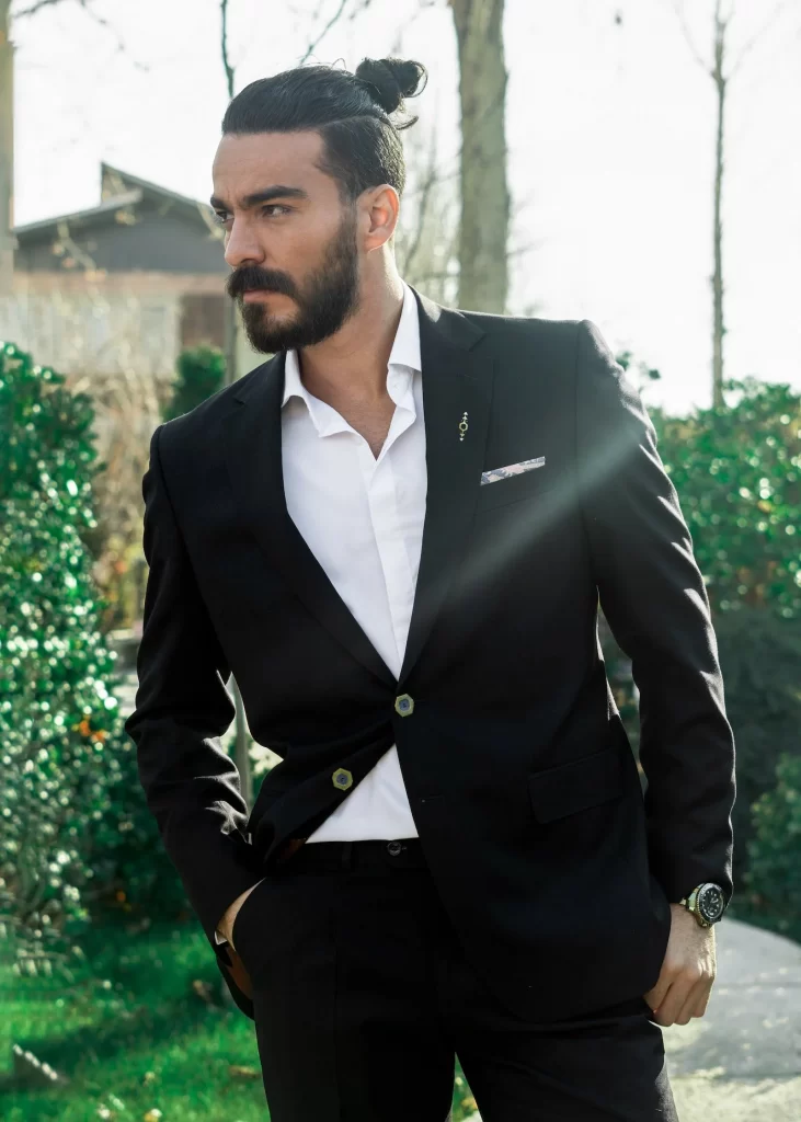 Groom with manbun and beard wearing black suit coat and white shirt with no tie, looks away from the camera