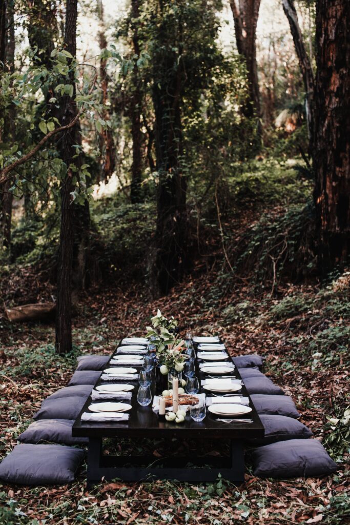 long low table set with plates and flowers,with cushions on ground in a forest