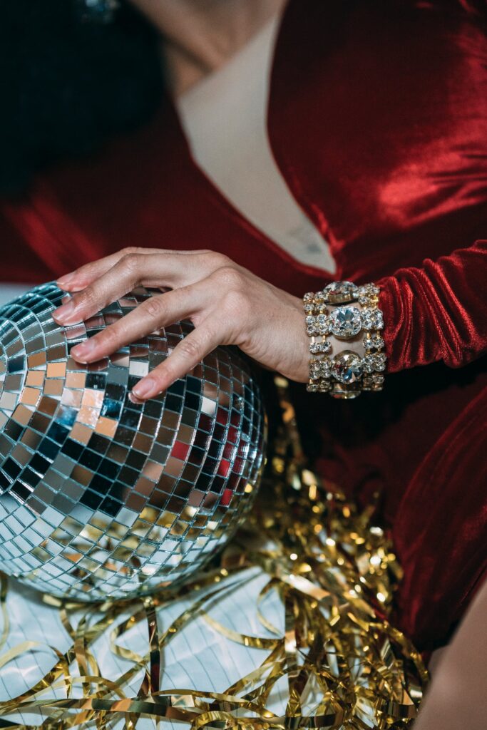 mirror ball, gold tinsel, held by woman with bulky bracelets and rich red velvet gown