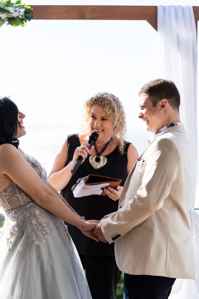 Laughing bride and groom with Lynette Maguire Marriage Celebrant standing under an arbour