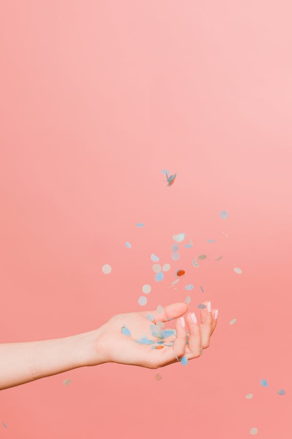 Woman's hand throwing coloured eco-confetti again a pink background