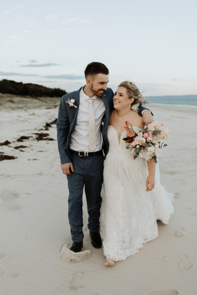 Bride and groom walking with big smiles and barefoot on a beach