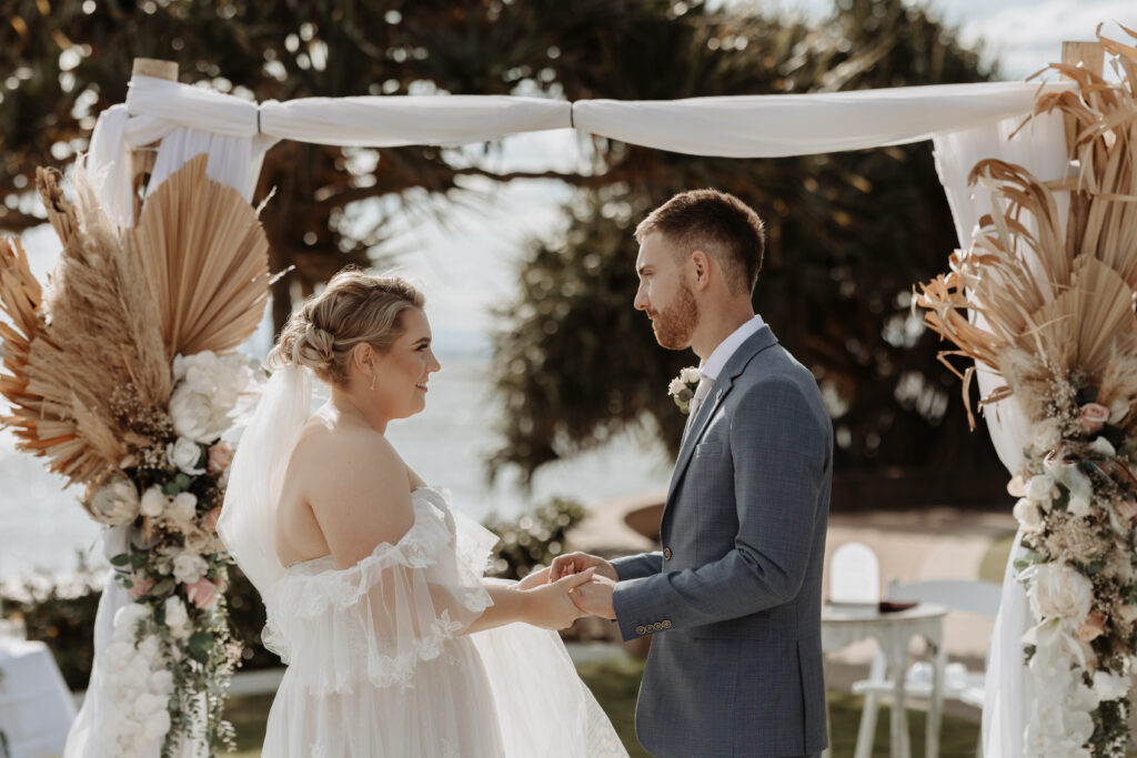 Happy bride and groom standing holding hands under eco-friendly arbor 